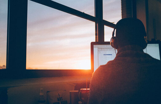 man in front of computer with sunset outside window