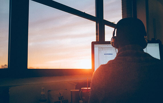 man in front of computer with sunset outside window