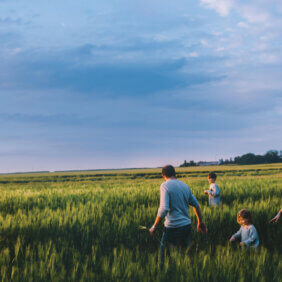 Family with three boys walking through the barley field - watch Fightback Farmers: Feeding Australia Together on the ABC.