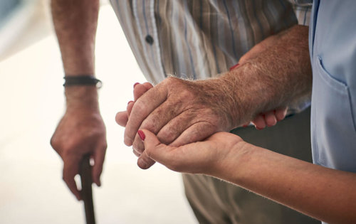 Close up of carer supporting patient by hand, aged care, istock