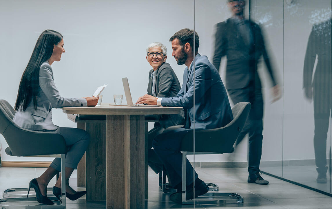 Shot of a group of business people having a meeting in board room. Businessman walking in blurred motion around his colleagues. Group of entrepreneurs on meeting in board room. Corporate business team on meeting in the office. The view is through glass.